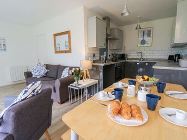 An open-plan kitchen and living area with a dining table set with croissants and cups at 17 Coedrath Park Saundersfoot