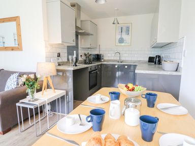 A kitchen and dining area with a table set with mugs plates and croissants at 17 Coedrath Park in Saundersfoot