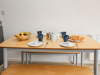 A dining table set with blue mugs, white plates, croissants, a fruit bowl, and a metal teapot at 17 Coedrath Park Saundersfoot
