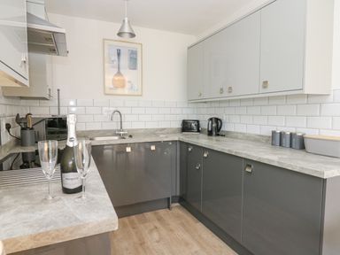 A kitchen with grey cabinets a bottle of prosecco two glasses a kettle toaster and containers on the countertop at 17 Coedrath Park Saundersfoot