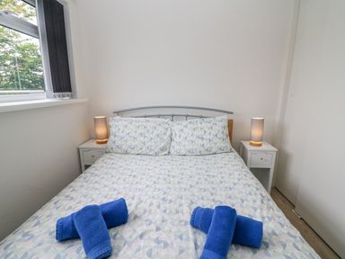 A bedroom with a double bed with patterned bedding blue towels on the bed two bedside tables with lamps and a window with vertical blinds at 17 Coedrath Park in Saundersfoot