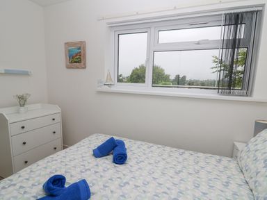 A bedroom with a bed with patterned bedding and blue towels a white chest of drawers and a window with a view at 17 Coedrath Park in Saundersfoot