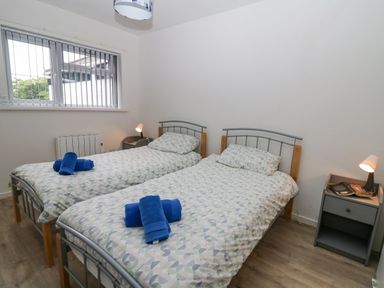 A bedroom with two single beds side by side with patterned bedding and blue towels on top at 17 Coedrath Park in Saundersfoot