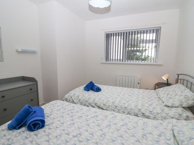 A bedroom with two single beds with patterned bedding blue towels on each bed a gray chest of drawers and a window with vertical blinds at 17 Coedrath Park Saundersfoot
