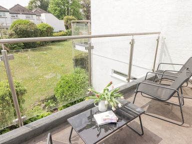 A balcony with two chairs and a table with a vase of flowers overlooking a garden at 28 Coedrath Park in Saundersfoot