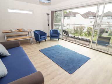 A living room with a sofa two armchairs a dining table with benches and a blue rug at 28 Coedrath Park Saundersfoot