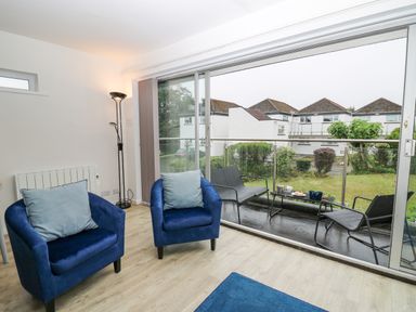A sitting area with two blue chairs inside and a balcony with black chairs and table outside at 28 Coedrath Park in Saundersfoot