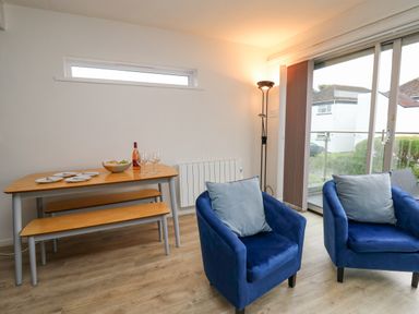 A dining area with a wooden table and benches and two blue armchairs near glass sliding doors at 28 Coedrath Park in Saundersfoot