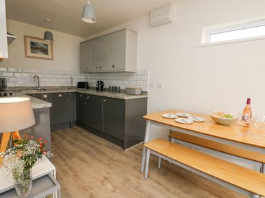 A kitchen with grey cabinets a wooden dining table with benches and dishes at 28 Coedrath Park Saundersfoot