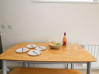 A dining table with four plates each with a knife a bowl with bread and grapes a bottle of wine and four wine glasses at 28 Coedrath Park Saundersfoot