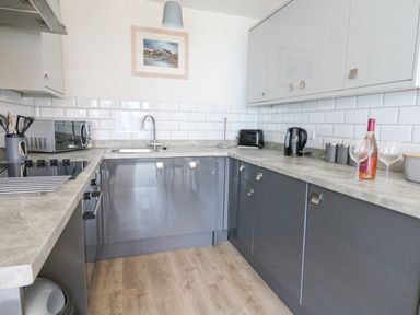 A kitchen with grey cabinets countertop white tiled backsplash sink toaster kettle microwave and wine bottle at 28 Coedrath Park Saundersfoot
