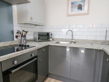 A kitchen with grey cabinets a built-in oven a microwave a sink and cooking utensils at 28 Coedrath Park Saundersfoot