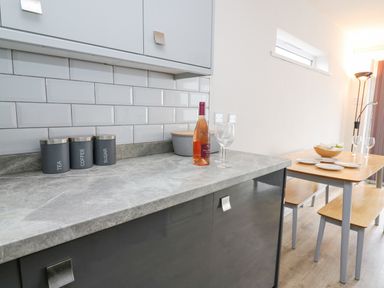 A kitchen countertop with containers labeled tea coffee and sugar and a dining table with plates and glasses at 28 Coedrath Park in Saundersfoot