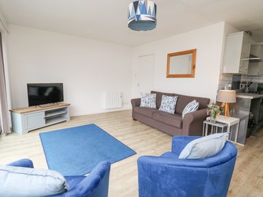 A living room with a blue rug a sofa armchairs and a TV on a stand at 28 Coedrath Park Saundersfoot