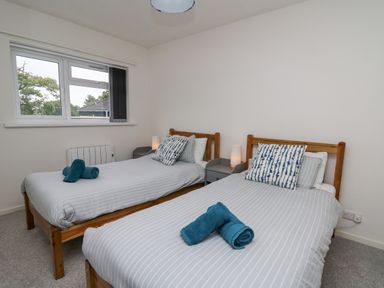 A bedroom with two single beds side by side with gray striped bedding and blue pillows at 28 Coedrath Park in Saundersfoot