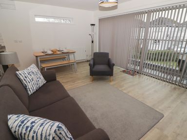 A living room with a sofa, armchair, dining table with benches, floor lamp, and vertical blinds at 26 Coedrath Park in Saundersfoot