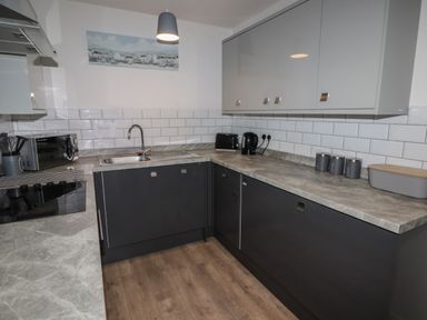 A kitchen with gray cabinets gray countertops a stainless steel sink a microwave kettle toaster and storage canisters on the counter at 26 Coedrath Park Saundersfoot