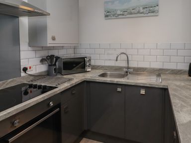 A kitchen corner with a stovetop oven microwave sink and tiled backsplash at 26 Coedrath Park Saundersfoot