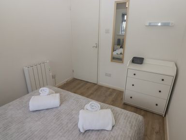 A bedroom with a bed with towels on it a white chest of drawers a mirror on the wall and a door at 26 Coedrath Park Saundersfoot