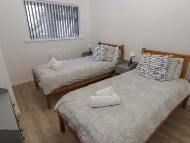 A bedroom with two single beds with striped bedding pillows and rolled towels beside a window at 26 Coedrath Park Saundersfoot