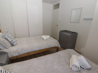 A bedroom with two single beds gray bedding a gray dresser a mirror and a closet at 26 Coedrath Park Saundersfoot