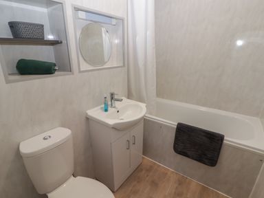 A bathroom with a toilet sink cabinet bathtub and shelves holding a towel and basket at 26 Coedrath Park Saundersfoot