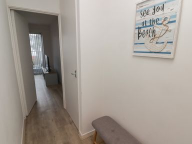 A hallway with wooden flooring a bench on the right and a wall decoration with an anchor and the words see you at the beach at 26 Coedrath Park Saundersfoot