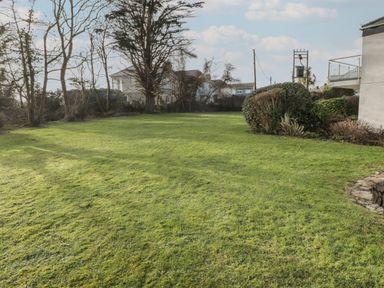 A backyard with grass lawn bushes and trees near houses at 26 Coedrath Park Saundersfoot