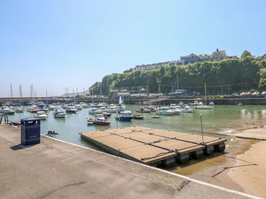 A harbor with boats moored in the water and a floating dock with a blue litter bin on the pavement at 26 Coedrath Park in Saundersfoot