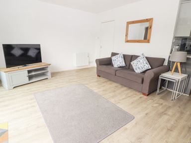 A living room with a brown sofa with two cushions a television on a stand a wooden framed mirror and a floor lamp at 26 Coedrath Park Saundersfoot