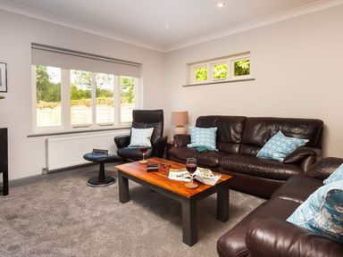 A living room with brown leather sofas a wooden coffee table and large windows at Bellman Cottage in Bowness-On-Windermere