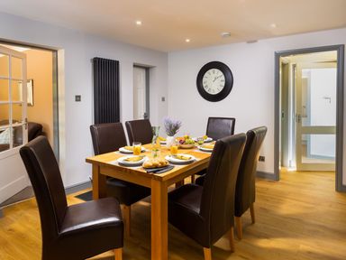 A dining room with a wooden table set for six with plates glasses and a centerpiece at Bellman Cottage in Bowness-On-Windermere