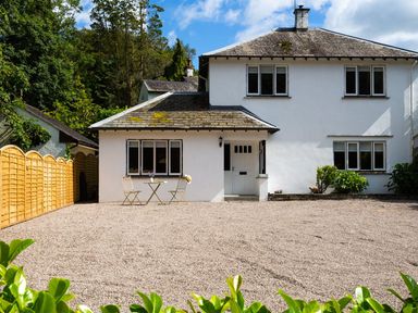 A white two-story house with a gravel front yard table and chairs outside and wooden fence on the left at Bellman Cottage in Bowness-On-Windermere