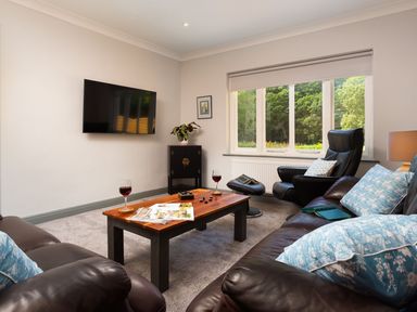 A living room with leather sofas a wooden coffee table and a wall-mounted television at Bellman Cottage in Bowness-On-Windermere