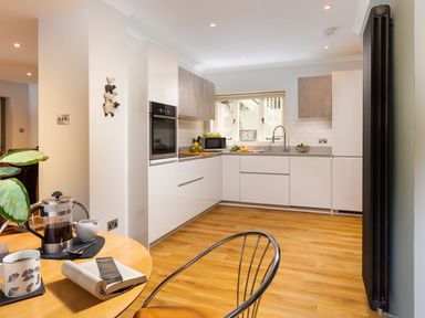 A kitchen with white cabinets wooden floor and a small round table with coffee and a book at Bellman Cottage in Bowness-On-Windermere