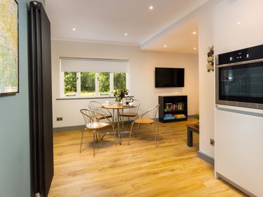 A dining area with a round table and four chairs near a window with a view of trees at Bellman Cottage in Bowness-On-Windermere