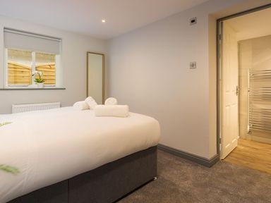 A bedroom with a bed topped with rolled towels a window with a potted plant a standing mirror and an open door leading to a bathroom at Bellman Cottage in Bowness-On-Windermere