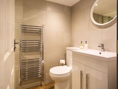 A bathroom with a toilet sink cabinet round mirror and heated towel rail at Bellman Cottage in Bowness-On-Windermere