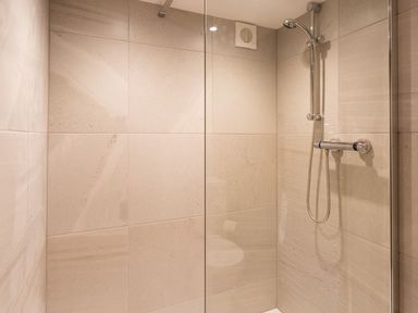 A shower area with wall tiles a handheld showerhead and a ventilation fan at Bellman Cottage in Bowness-On-Windermere
