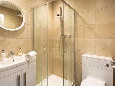 A bathroom with a shower enclosure a toilet a sink with soap dispensers and a round mirror at Bellman Cottage in Bowness-On-Windermere