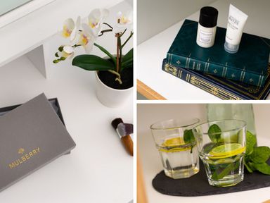 A white orchid plant in a white pot on a white surface with a Mulberry box and makeup brush two books with lotion bottles on top and two glasses of water with lemon and mint leaves at Bellman Cottage in Bowness-On-Windermere