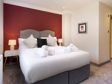 A bedroom with a double bed with pillows and rolled towels bedside tables with lamps and a painting on the wall at Bellman Cottage in Bowness-On-Windermere