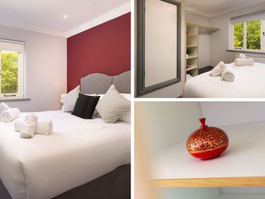A bedroom with a bed, pillows, rolled towels, window, shelving unit, and a small decorative red vase at Bellman Cottage in Bowness-On-Windermere