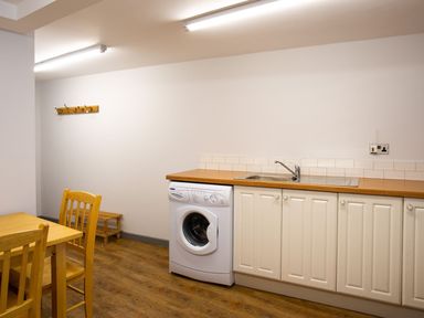 A kitchen area with a washing machine under a wooden countertop and white cabinets at Bellman Cottage in Bowness-On-Windermere