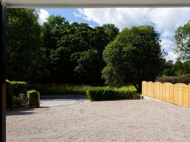 An outdoor gravel area with wooden fencing and trees at Bellman Cottage in Bowness-On-Windermere