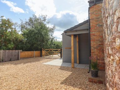 A gravel driveway with a wooden gate and a small porch attached to a brick and stone building at Bumblebee Cottage in East Nynehead near Bradford-On-Tone