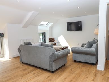 A living room with gray sofas a wooden chair a wall-mounted TV and wooden flooring at Bumblebee Cottage in East Nynehead near Bradford-On-Tone