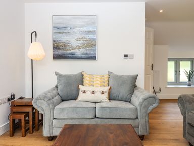 A living room with a grey sofa with patterned cushions a wooden coffee table a floor lamp and nested side tables with a painting on the wall at Bumblebee Cottage in East Nynehead near Bradford-On-Tone