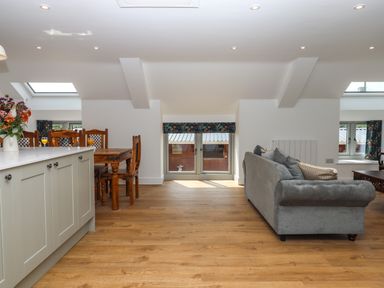 An open living and dining area with a wooden dining table and chairs a gray sofa and a kitchen island with flowers at Bumblebee Cottage in East Nynehead near Bradford-On-Tone