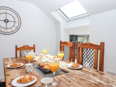 A dining table with wooden chairs set with croissants orange juice cups and a teapot under a skylight at Bumblebee Cottage in East Nynehead near Bradford-On-Tone